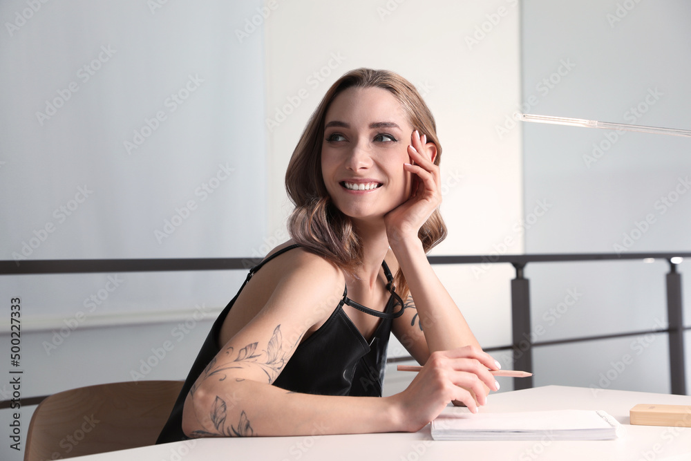 Beautiful woman with tattoos on body drawing in sketchbook at table indoors Beautiful woman with tattoos on body drawing in sketchbook at table indoors