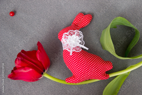 Red textile bunny and red tulip on gray background top view