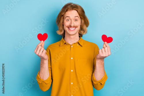Portrait of attractive cheerful long-haired guy holding in hands two cards amour isolated over bright blue color background