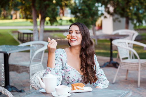 Beautiful long haired woman eating honey cake in the outdoor cafe in summer.