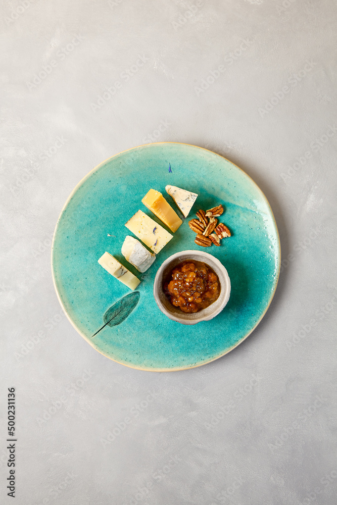 Cheese platter on blue ceramic plate. Cheeseboard on handmade dinner plate in modern style. Different cheese on ceramic dishware in minimal style.