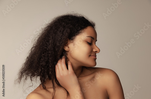 Close-up portrait of young beautiful woman with natural curly hair posing isolated over grey background