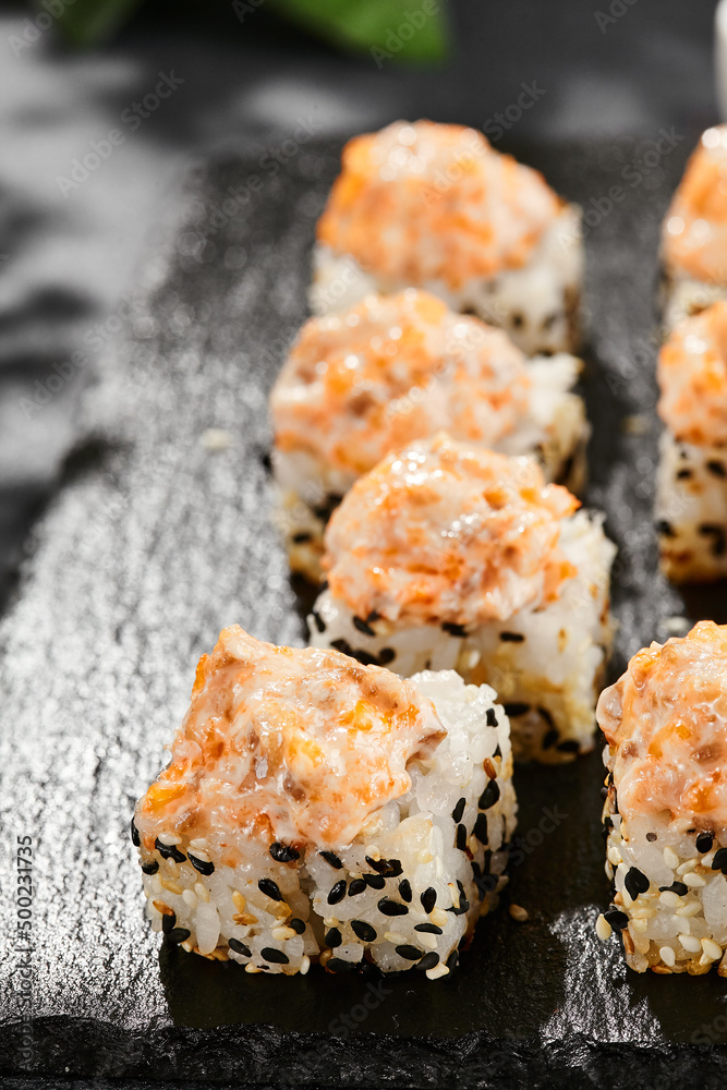 Baked Maki sushi on dark slate. Hot sushi roll with salmon and cheese. Sushi roll sesame outside, baked salmon and cheese topped. Style concept japanese menu with black background, leaves and shadow. Baked Maki sushi on dark slate. Hot sushi roll with salmon and cheese. Sushi roll sesame outside, baked salmon and cheese topped. Style concept japanese menu with black background, leaves and shadow.