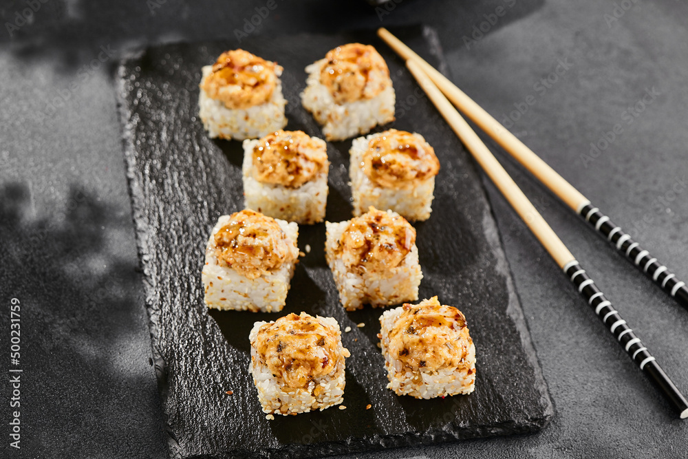 Baked Maki sushi on dark slate. Hot unagi maki with eel. Sushi roll with baked eel, cheese and unagi sauce topped. Style concept japanese menu with black background, leaves and hard shadow. Baked Maki sushi on dark slate. Hot unagi maki with eel. Sushi roll with baked eel, cheese and unagi sauce topped. Style concept japanese menu with black background, leaves and hard shadow.