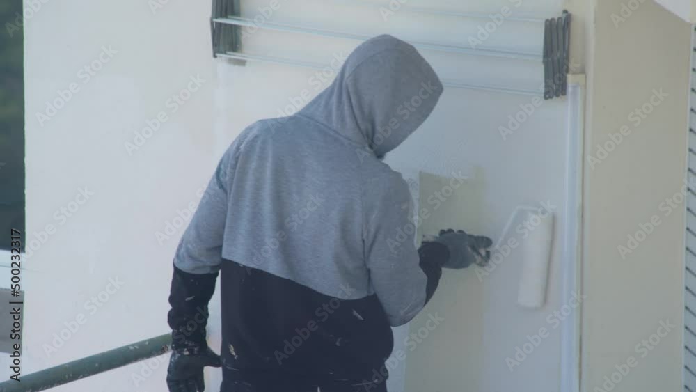 A professional painter on a lift paints the walls of a multi-storey building white. A professional painter on a lift paints the walls of a multi-storey building white.