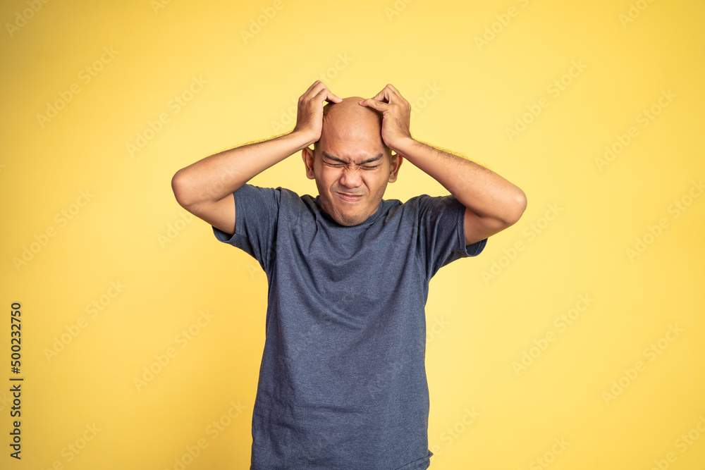Stressed asian bald young man holding head on isolated background Stressed asian bald young man holding head on isolated background