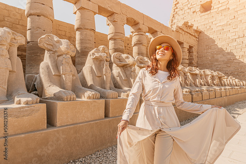 A happy tourist girl interested in Egyptology and archaeology and gets a travel experience at the Karnak Temple in Luxor among alley of sphinxes in Thebes