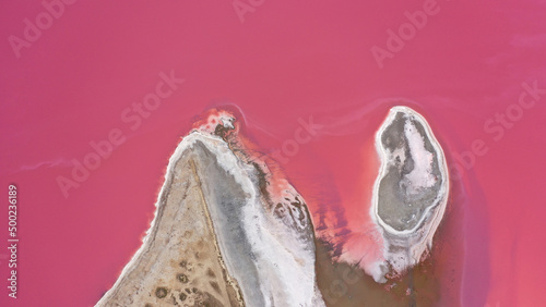 Flying over a pink salt lake. Salt production facilities saline evaporation pond fields in the salty lake. Dunaliella salina impart a red, pink water in mineral lake with dry cristallized salty coast.