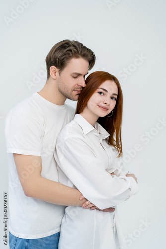 Young man hugging smiling redhead girlfriend isolated on white.