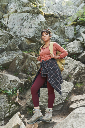 Portrait of serious young female climber with backpack and shirt wrapped around waist standing on stone