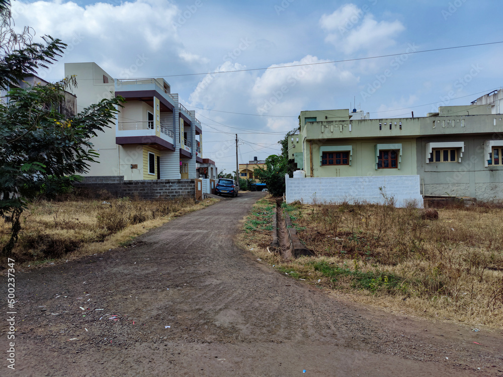 Scenic view of residential colony in Kolhapur city. cluster of apartment buildings and houses, green trees parked vehicles on the side of the empty asphalt road. Scenic view of residential colony in Kolhapur city. cluster of apartment buildings and houses, green trees parked vehicles on the side of the empty asphalt road.