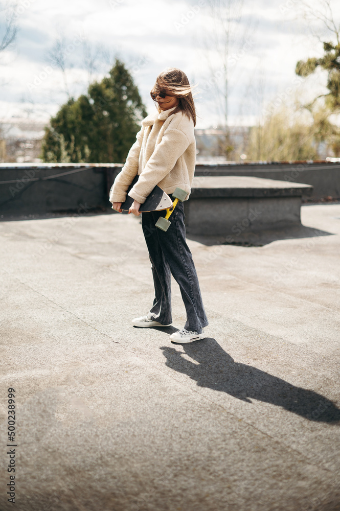 Stylish woman holding skateboard while standing on roof