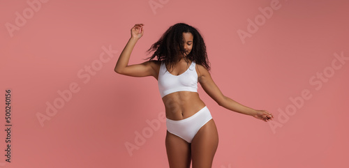 Portrait of cheerful young woman in white underwear posing dancing isolated over pink studio background