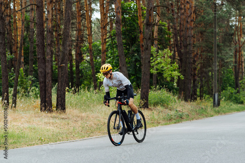 Handsome young male cyclist trains outside the city in the woods on the road. Riding a bike. © bodnarphoto