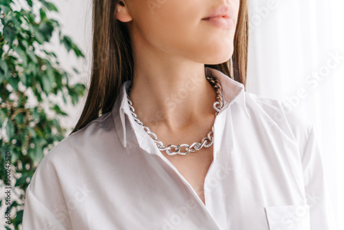 Silver bijouterie chain on woman neck. White blouse.