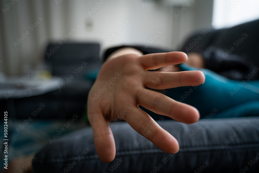 Young woman lying on sofa and holding hand to camera to protect herself because she is scared
