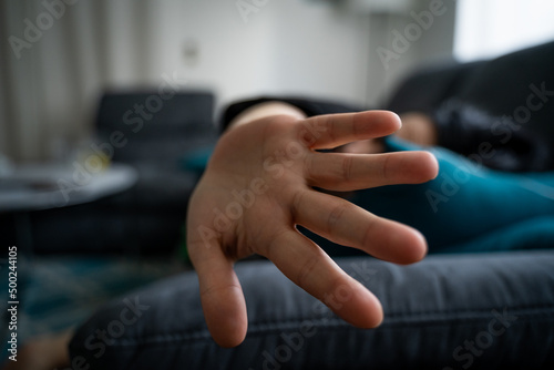 Young woman lying on sofa and holding hand to camera to protect herself because she is scared