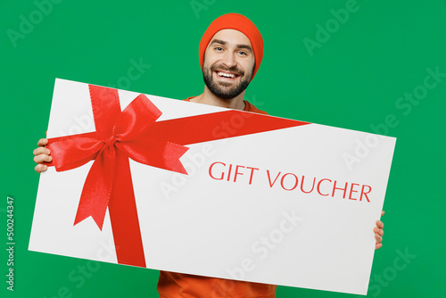 Young smiling cool happy caucasian man 20s in orange sweatshirt hat hold big gift certificate coupon voucher card for store isolated on plain green background studio portrait People lifestyle concept