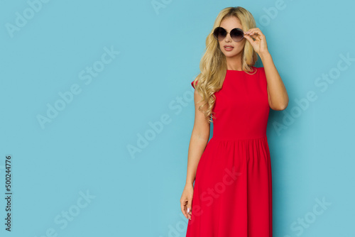 Beautiful blond woman is posing in red cocktail dress and sunglasses.