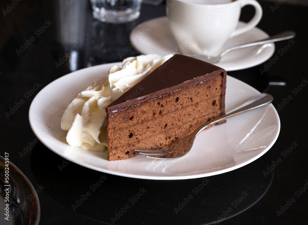 Piece of famous Sachertorte chocolate cake with apricot jam of Austrian origin served with whipped cream Piece of famous Sachertorte chocolate cake with apricot jam of Austrian origin served with whipped cream