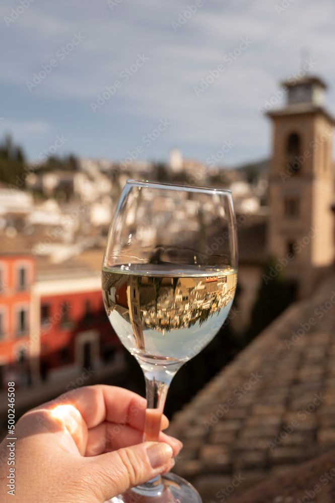 Hand with glass of Spanish dry rueda white wine on roof terrace with view on old part of Andalusian town Granada, Spain