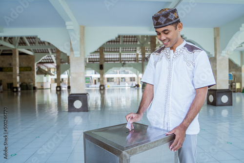 portrait of male muslim paying some zakat charity using cash at the mosque. indonesian money rupiah bank note for zakat photo