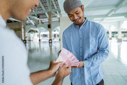 portrait of male muslim paying some zakat charity using cash at the mosque. indonesian money rupiah bank note for zakat photo