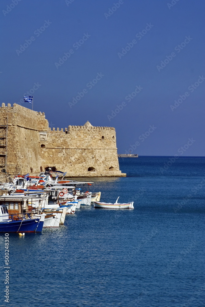 Fishing boats in the harbor below the walls of a stone fortress on Crete, Greece