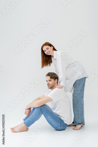 Smiling woman looking at camera while standing near boyfriend on white background.
