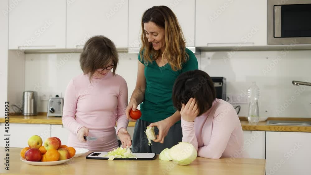 Two girls with Down Syndrome are learning to cook with their mother in kitchen at home Two girls with Down Syndrome are learning to cook with their mother in kitchen at home