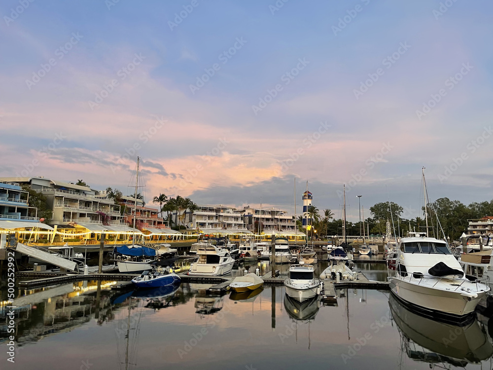 Phuket Boat Lagoon yacht club. Beautiful pink sunset above sea harbor, reflection on the surface of water. Luxury yachts, sailboats, speedboats. Buildings on the embankment. Moored vessels. Sailing