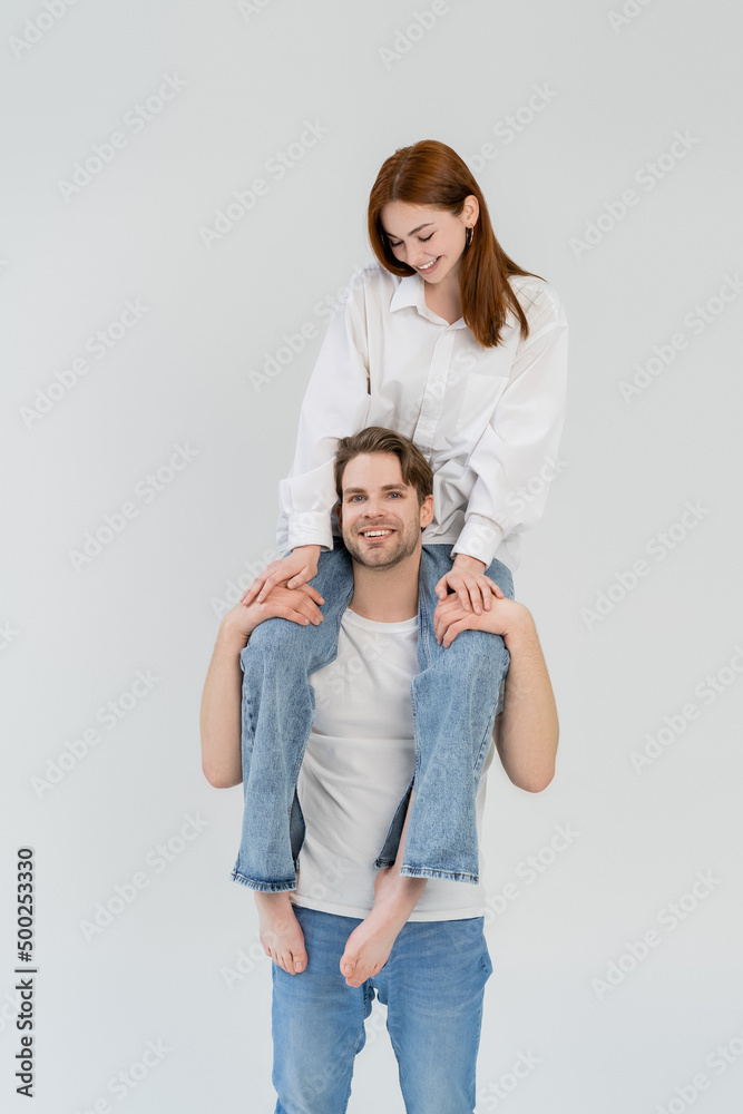 Cheerful man holding barefoot girlfriend on shoulders isolated on white. Cheerful man holding barefoot girlfriend on shoulders isolated on white.