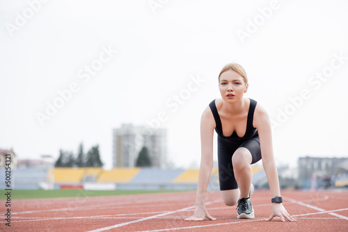 young sportswoman looking at camera while standing in low start position on stadium.