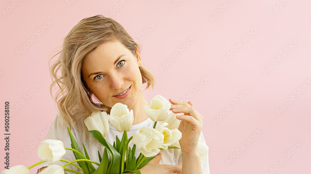 The concept of spring, happiness and holiday. Close-up portrait of a beautiful smiling girl holding a bouquet of white tulips in her hands looks straight in on a pink background