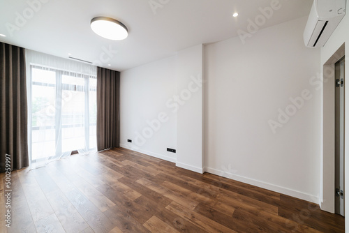 Large  new  empty room with white walls and wood floors. Large window in the room