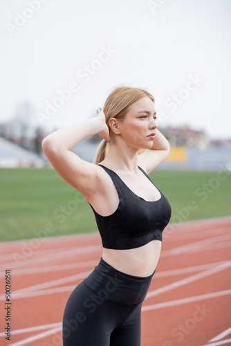 young sportive woman warming up with hands behind head outdoors.
