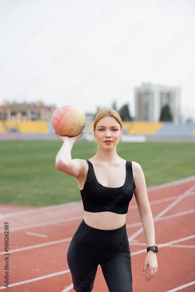 young sportive woman with ball looking at camera on stadium.