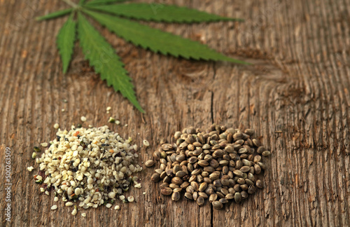 Two heaps of raw hemp seeds, whole and shelled, and cannabis leaf against a background of wood texture. Selective focus.