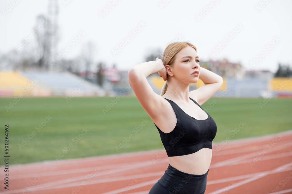 young sportive woman in black sports bra warming up with hands behind head.  Stock Photo
