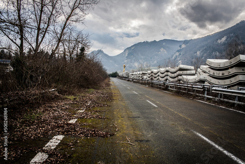 Blocchi di cemento abbandonati lungo una strada sul cui altro ciglio c'è della vegetazione spoglia e sullo sfondo le montagne ed un cielo grigio. photo