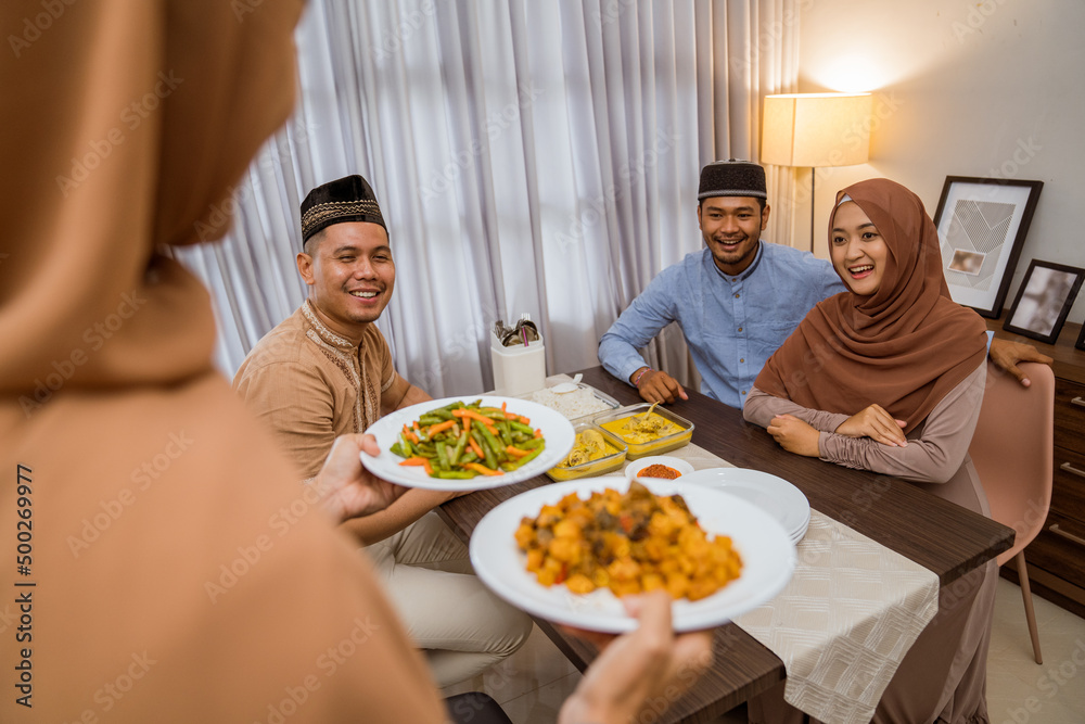 excited asian muslim woman served the food for friend while sitting on dining table for iftar or eid mubarak gathering at home