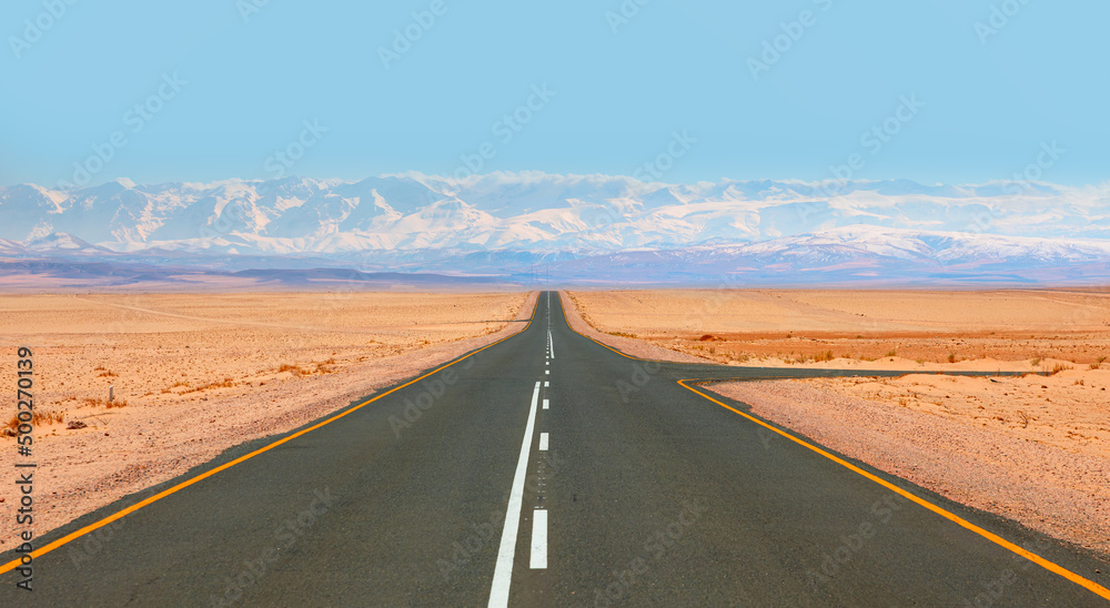 Empty road runs through a scenic national park and towards the snowy mountains in the distance.