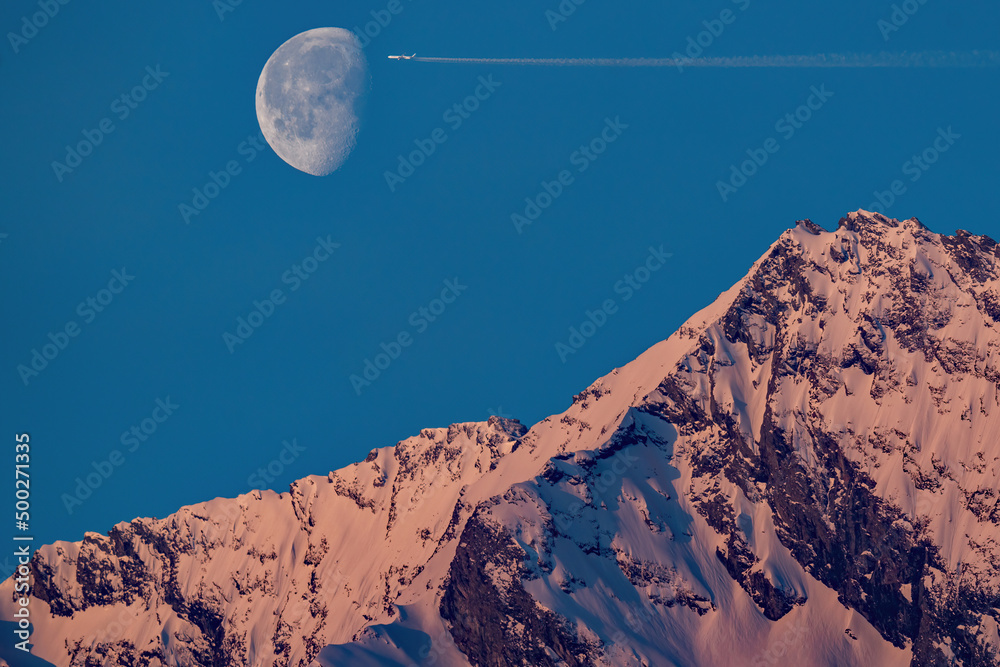 sunrise and moonset over the snowcapped alps, the hohe tauern in the national park, with airplane front of the moon on the clear blue sky