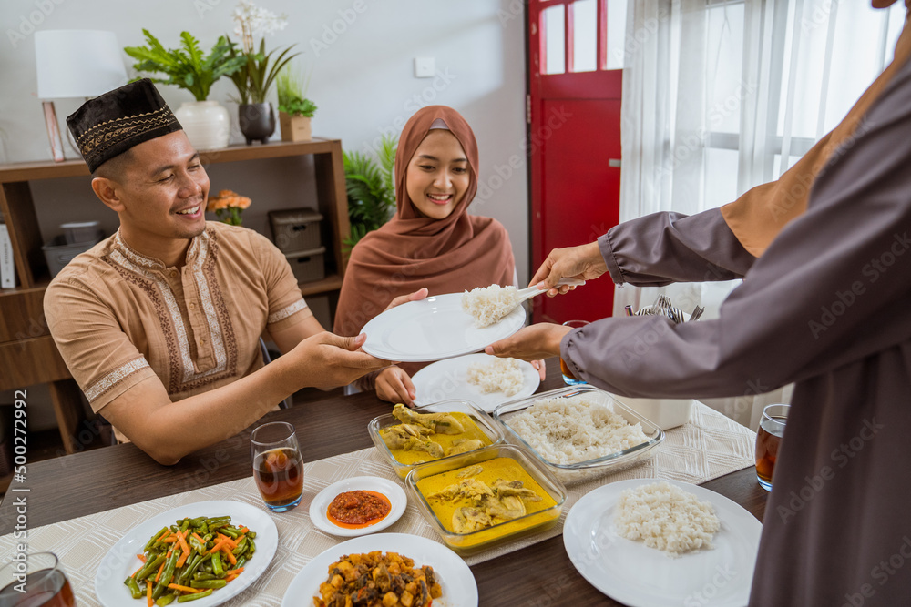 excited asian muslim woman served the food for friend while sitting on dining table for iftar or eid mubarak gathering at home excited asian muslim woman served the food for friend while sitting on dining table for iftar or eid mubarak gathering at home