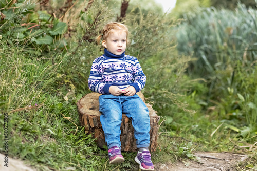 A little girl toddler is sitting on a stump in a spring park. Walk