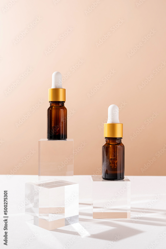 Amber glass dropper bottles with a pippette with white rubber tip on glass podium and beige background, mockup design Amber glass dropper bottles with a pippette with white rubber tip on glass podium and beige background, mockup design