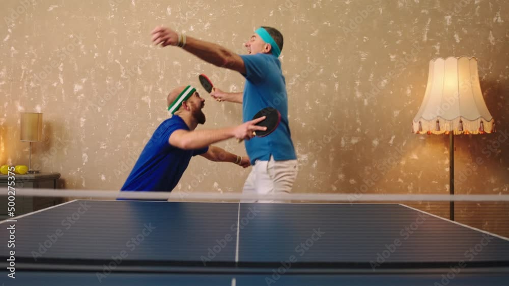 Two charismatic men one young and one old happy playing the table tennis or ping pong they they hitting ball with the racket and hugging each other