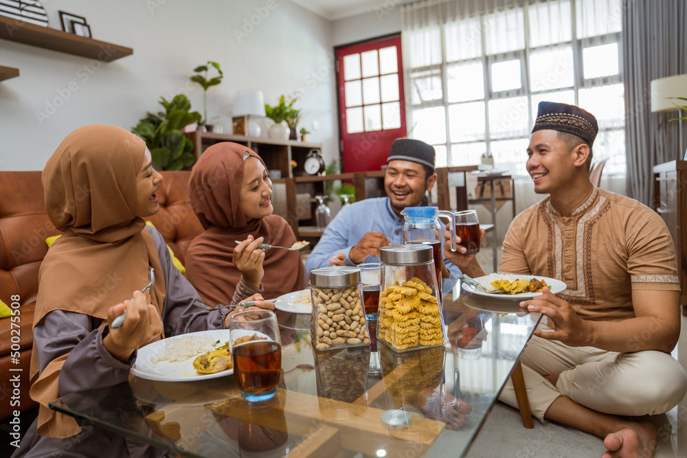 asian muslim friend having iftar dinner together while sitting on the floor in the livingroom asian muslim friend having iftar dinner together while sitting on the floor in the livingroom