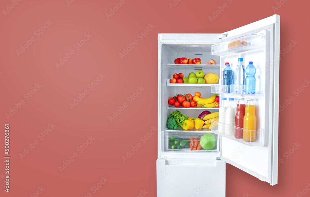Open fridge full of vegetables, fruits and drinks on pink wall background. Copy space