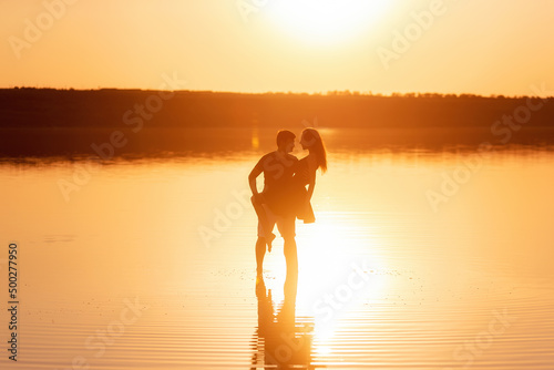 Silhouette of a couple in love, dances with splashes in the water of the lake in the orange sunset